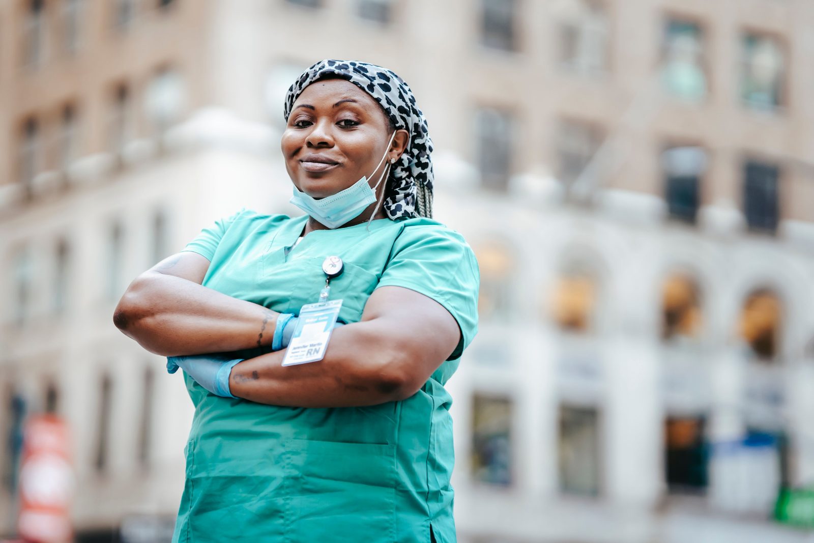 A registered nurse in scrubs standing in front of New York City buildings