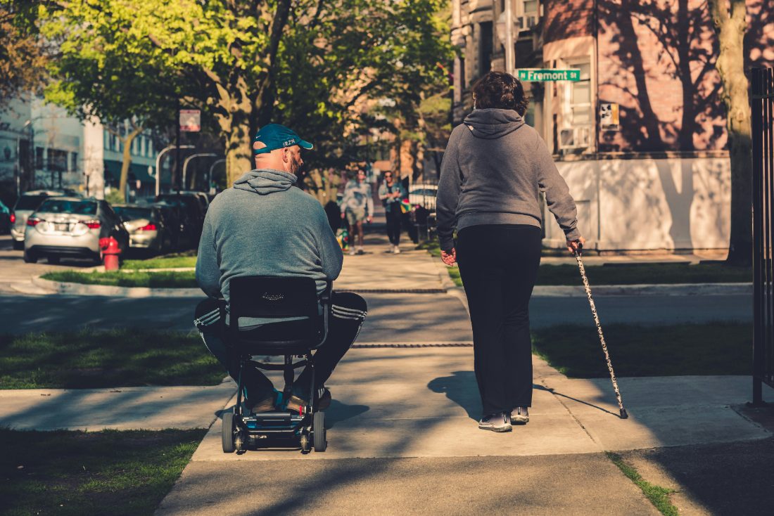 A person on a mobility scooter moving along a path beside a walking companion
